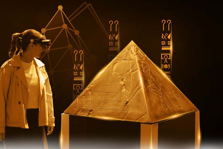 Visitor wearing a mixed-reality headset beside a golden pyramidion